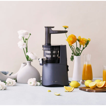 Hurom HA-2600 Classic Series slow juicer displayed alongside fruits and flowers, emphasizing its color and design.
